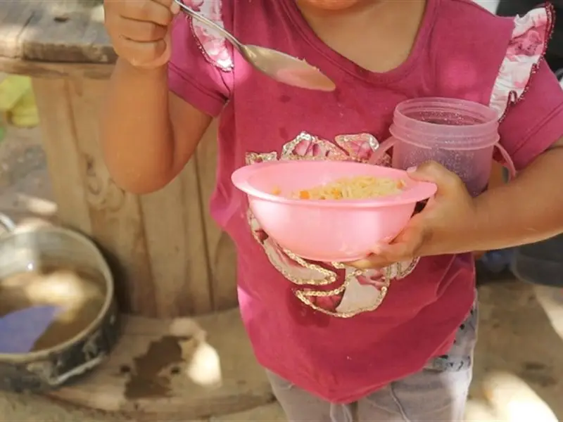 Criança segurando um prato de comida e um copo